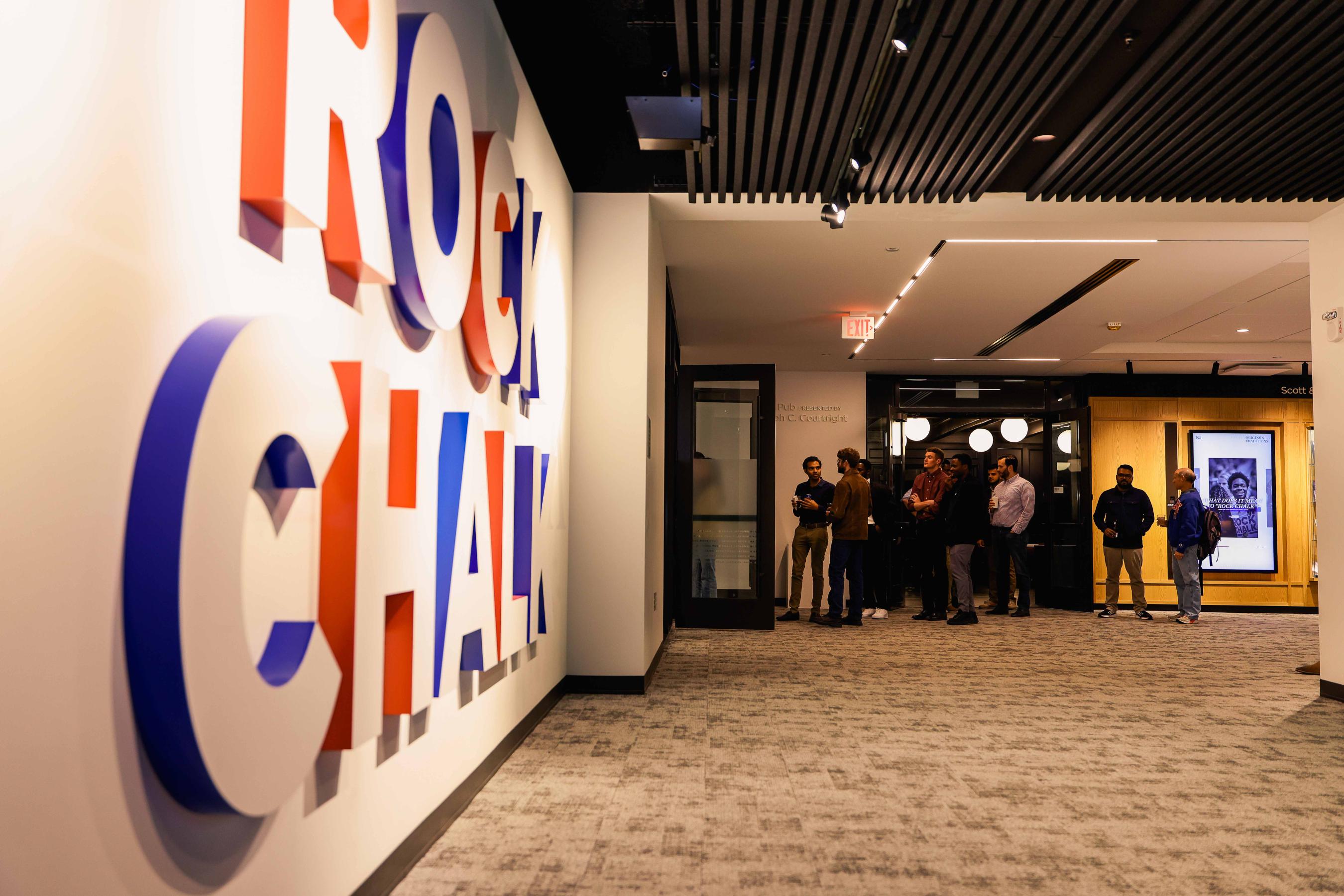 A modern hallway or lobby area with stylized text or logo on the wall and people visible in the background.