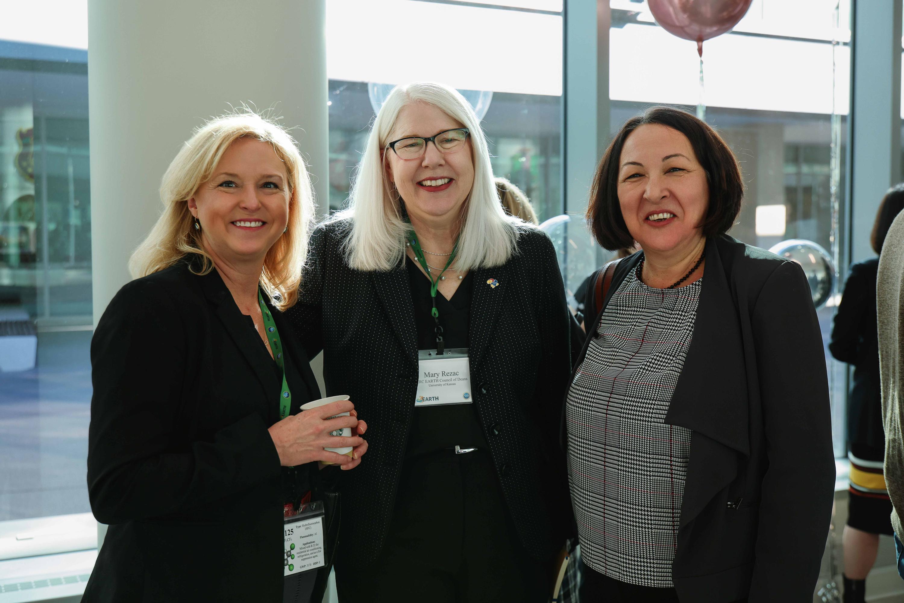 Three women in business attire standing together at a networking event, all wearing name badges